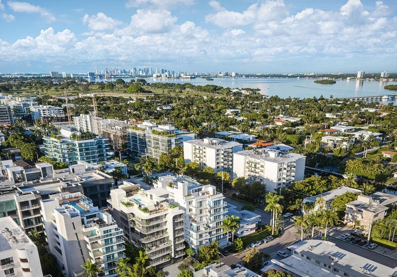 Aerial neighborhood view around Alma Bay Harbor in Bay Harbor Islands, Miami, with Biscayne Bay and a distant skyline, highlighting luxury and ultra luxury preconstruction condos in a peaceful waterfront enclave.