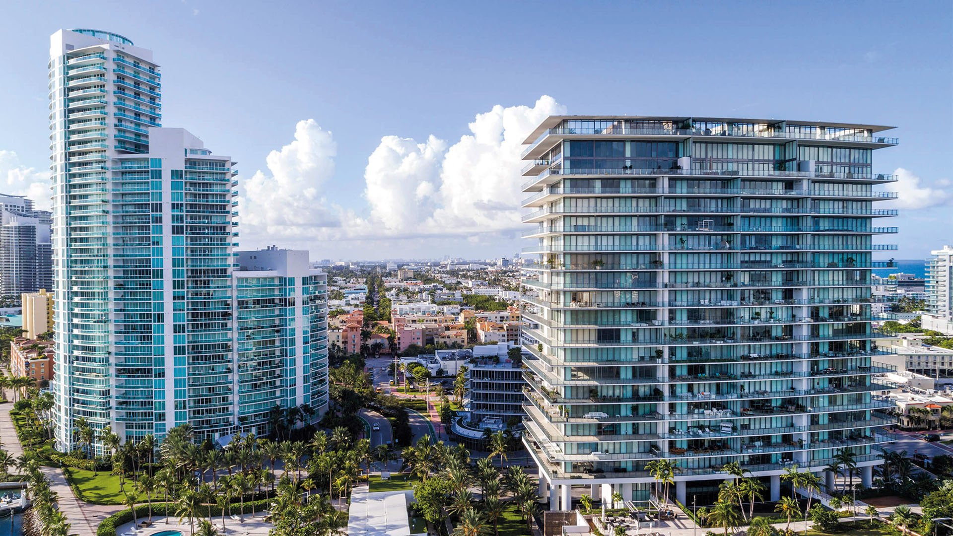 Aerial view of the glassy Apogee condo exterior and palm-lined grounds in South Beach, showcasing luxury and ultra luxury condos near the waterfront and skyline.