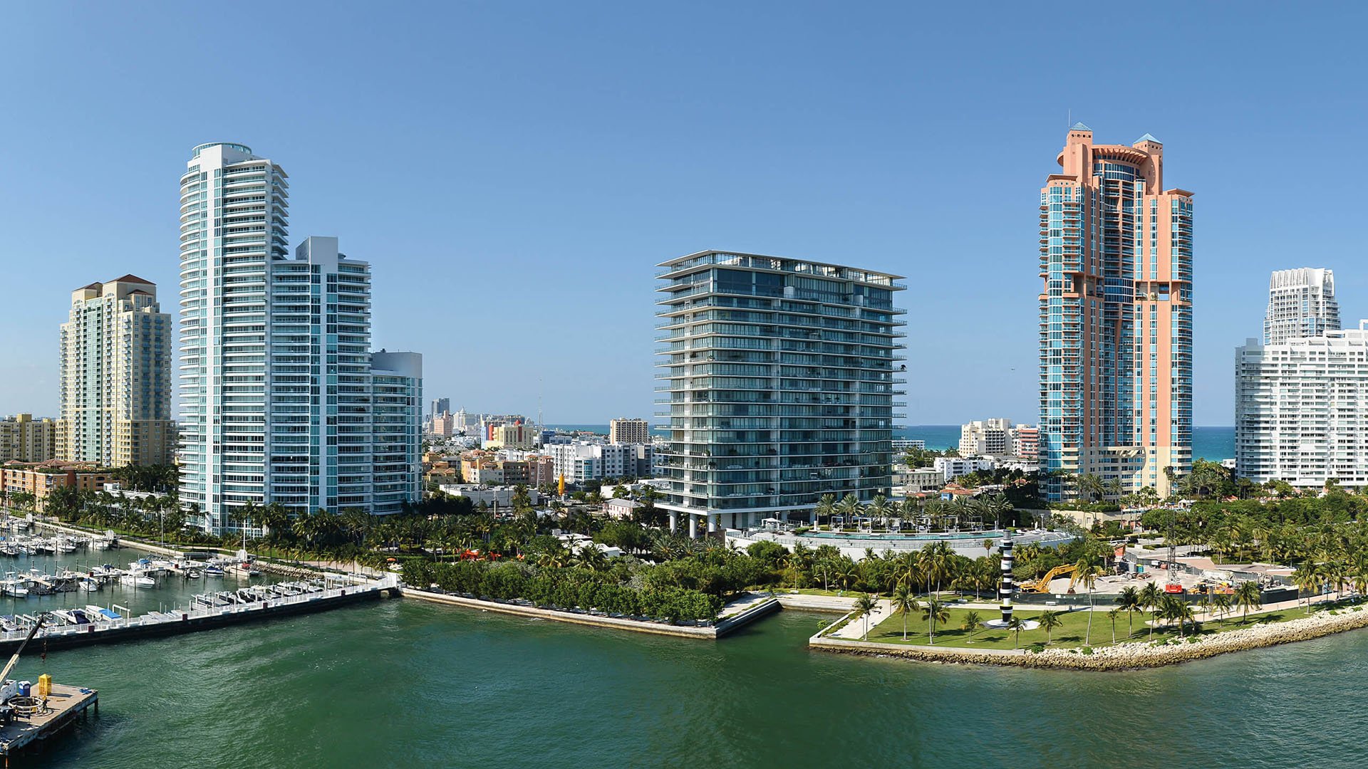 Aerial waterfront view of the Apogee tower beside a marina and neighboring high-rises in South Beach, highlighting luxury and ultra luxury condos on a prime bayfront setting.