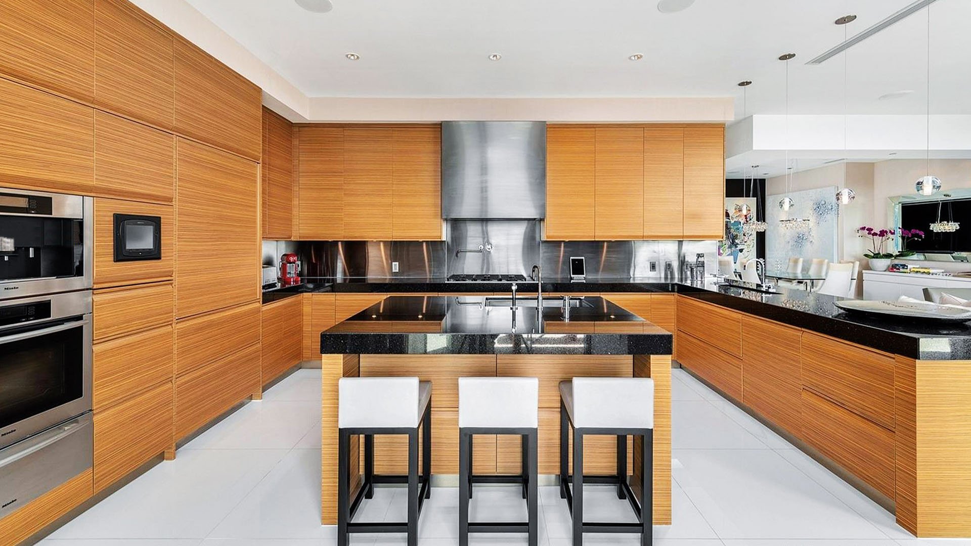 Chef kitchen with a black island, bar seating, wood cabinetry and stainless backsplash at Apogee in South Beach, highlighting luxury and ultra luxury condos interiors.