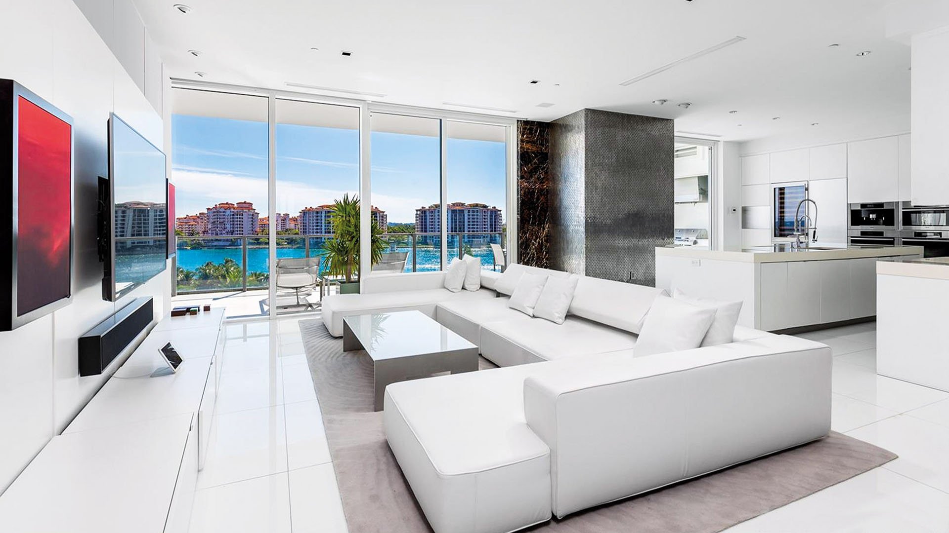 Open-plan living room and chef kitchen with white finishes, floor-to-ceiling glass and water views at Apogee in South Beach, showcasing luxury and ultra luxury condos interiors.