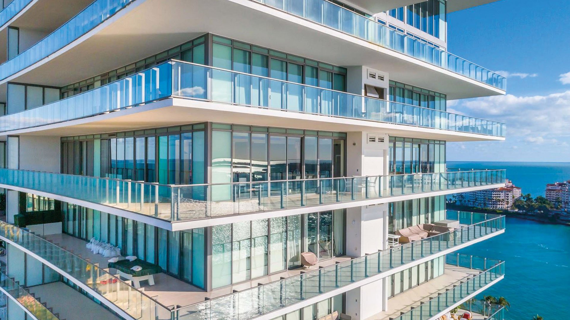 Close view of Apogee in South Beach with expansive wraparound glass balconies and blue water beyond, showcasing luxury and ultra luxury condos with oversized outdoor living.