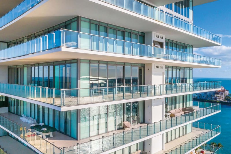 Close view of Apogee in South Beach with expansive wraparound glass balconies and blue water beyond, showcasing luxury and ultra luxury condos with oversized outdoor living.