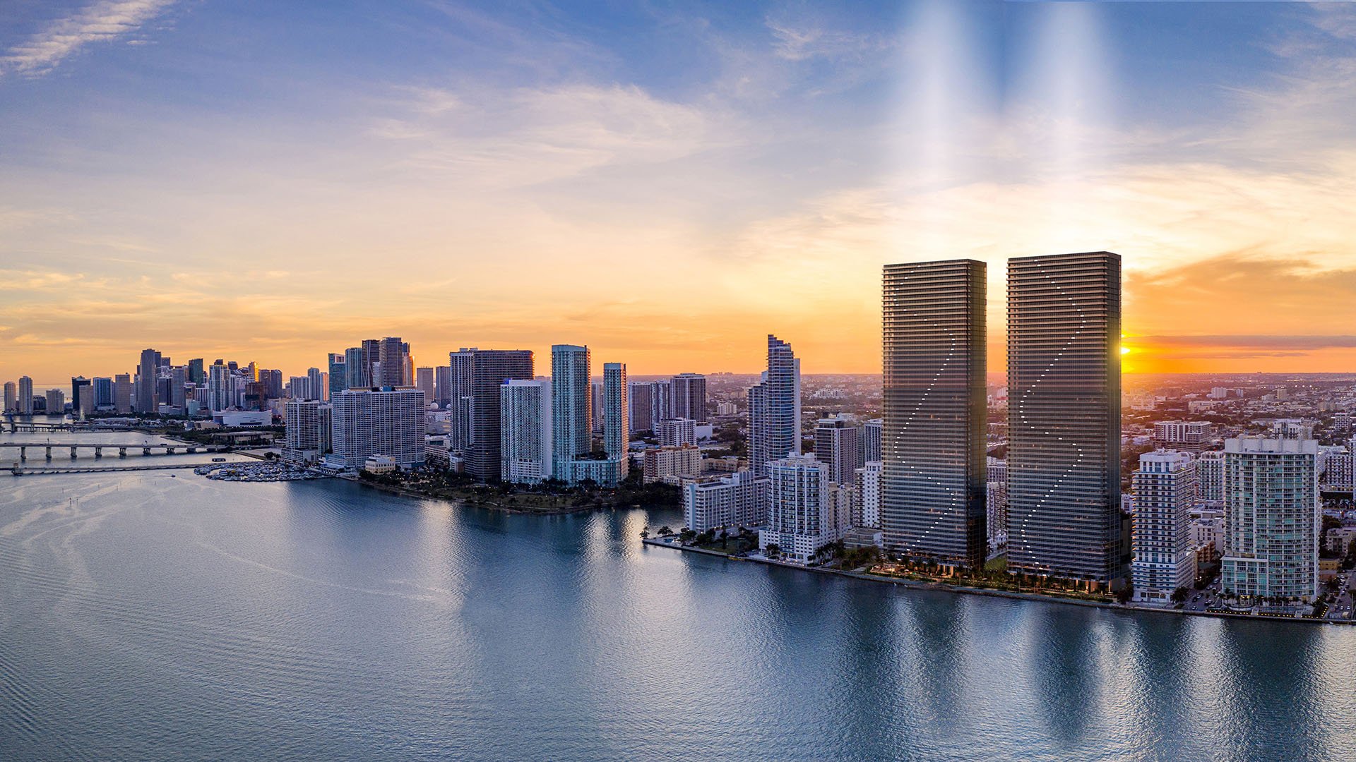 Aria Reserve Edgewater Miami dusk skyline with twin towers glowing at sunset over Biscayne Bay and Downtown Miami, showcasing luxury and ultra luxury preconstruction condos on the bayfront.