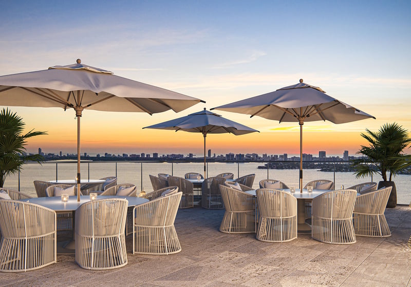 Aria Reserve Edgewater Miami rooftop dining terrace at sunset overlooking Biscayne Bay, featuring luxury and ultra luxury preconstruction condos with outdoor seating, umbrellas, and skyline water views.