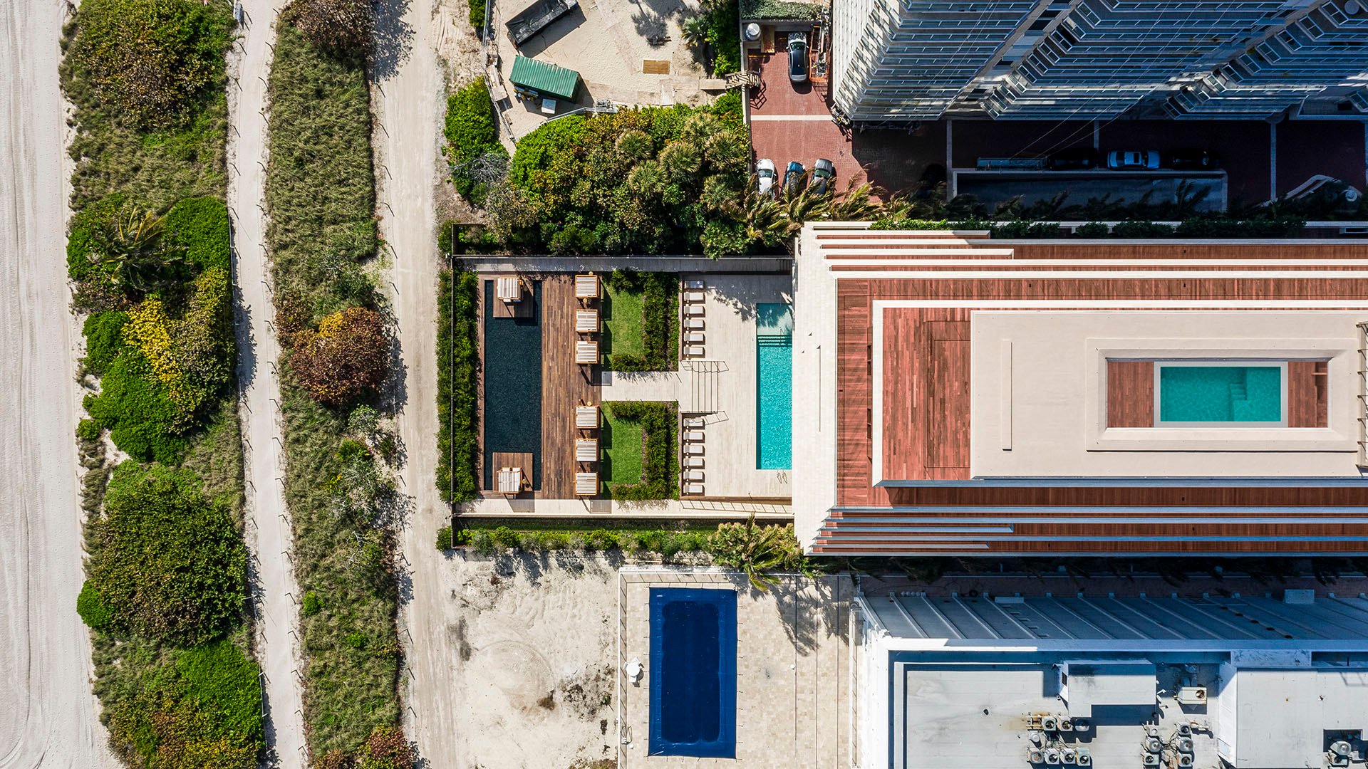 Aerial waterfront view of Arte Surfside, Surfside, Florida, showing luxury and ultra luxury condos with the rooftop structure, pool deck, cabanas, and the beach edge alongside the building.