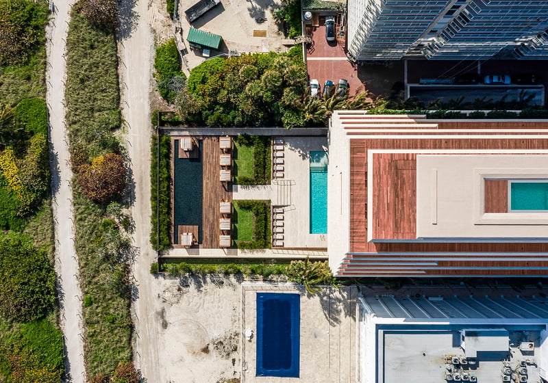 Aerial waterfront view of Arte Surfside, Surfside, Florida, showing luxury and ultra luxury condos with the rooftop structure, pool deck, cabanas, and the beach edge alongside the building.