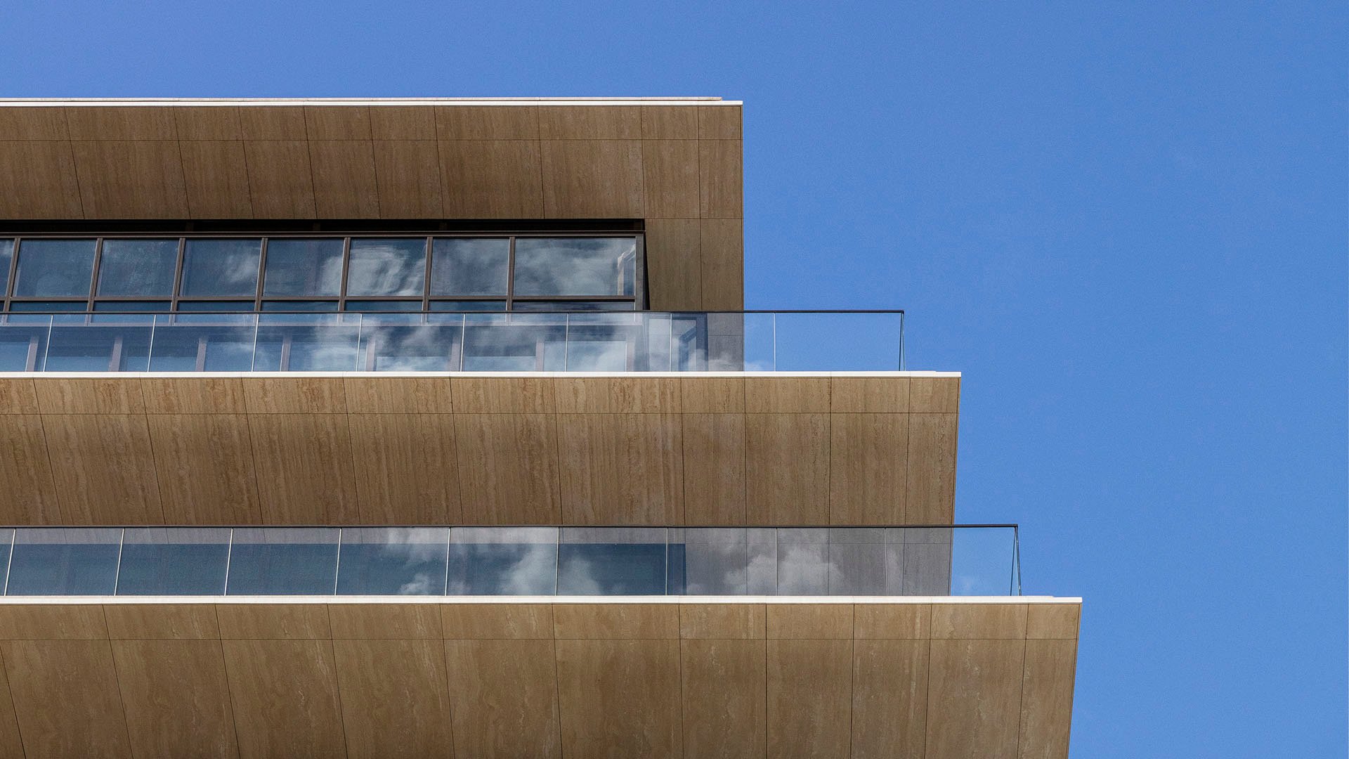 Facade closeup at Arte Surfside, Surfside, Florida, featuring luxury and ultra luxury condos with stacked stone terraces, glass railings, and a crisp modern exterior against the sky.
