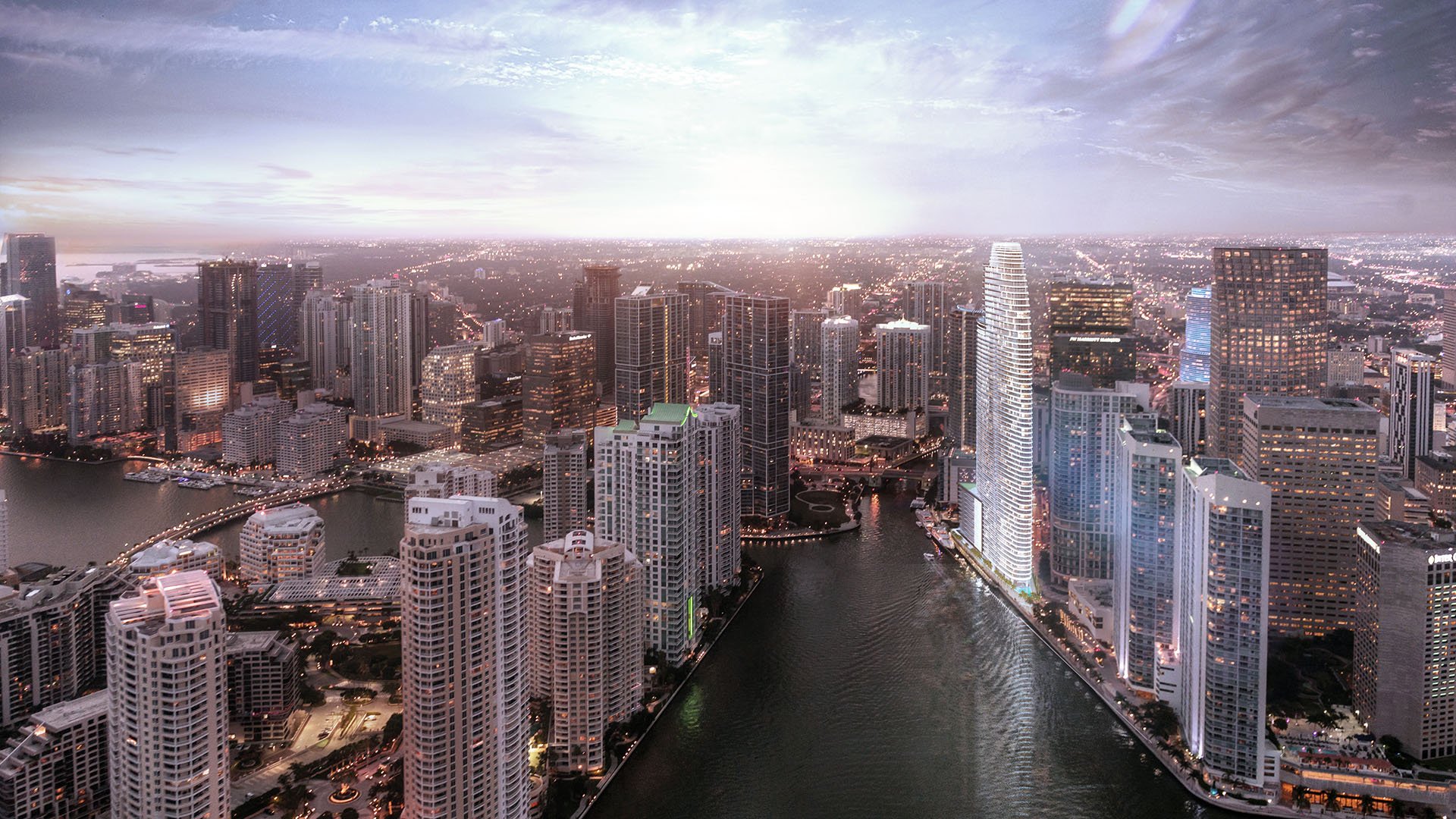 Aston Martin Residences in Downtown Miami luxury and ultra luxury condos aerial dusk view above the waterfront skyline, showing the curved tower glowing along the Miami River.