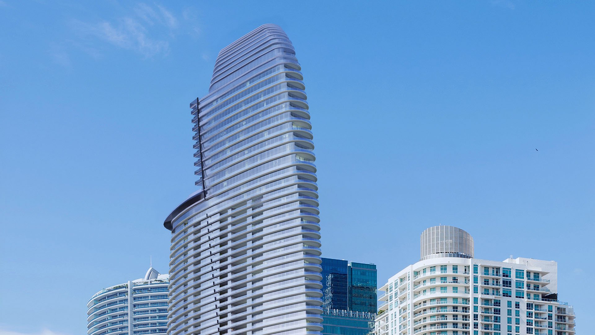 Aston Martin Residences in Downtown Miami luxury and ultra luxury condos exterior view of the curved tower against a clear blue sky above surrounding downtown buildings.