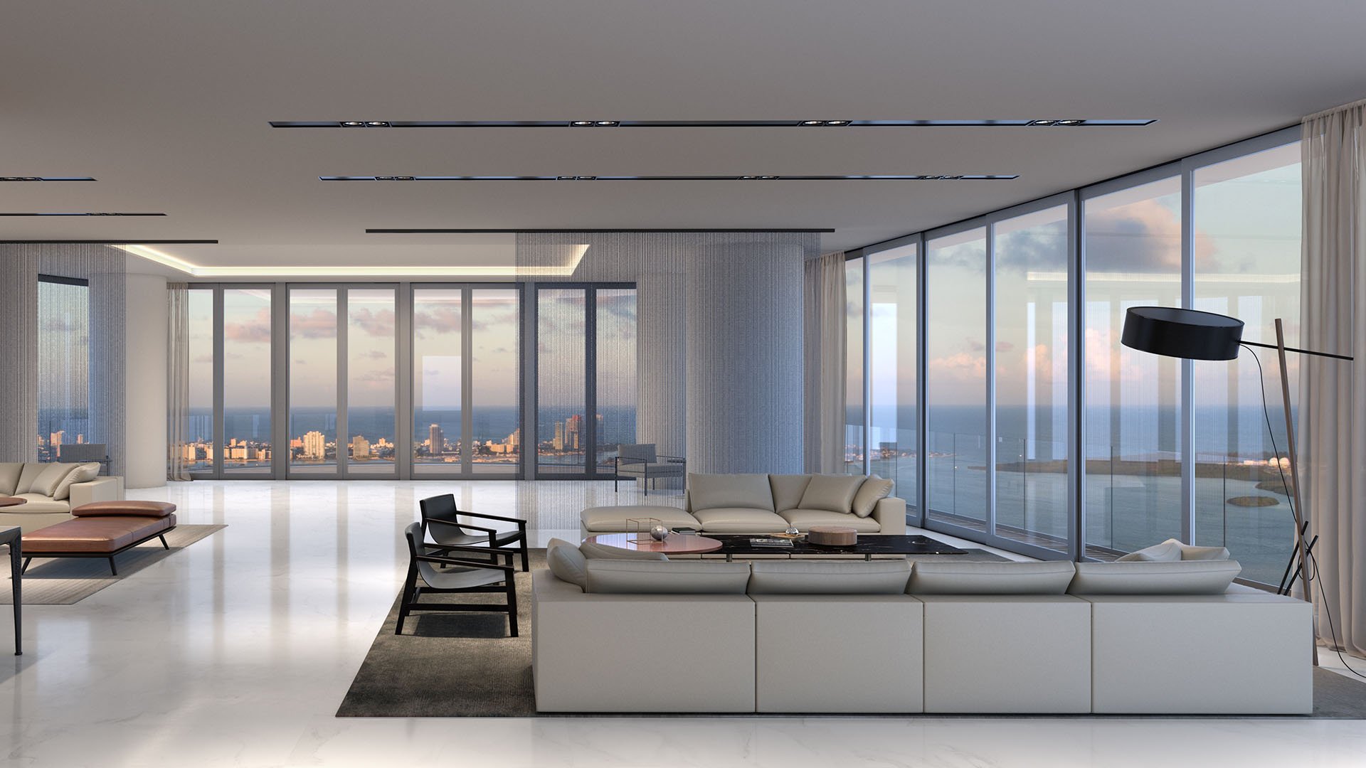 Aston Martin Residences in Downtown Miami luxury and ultra luxury condos expansive living room with wraparound glass, white seating, and wide water views at dusk.