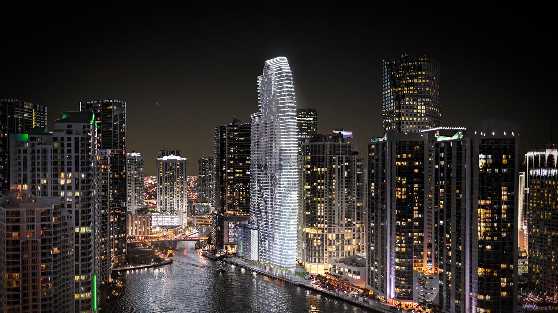 Aston Martin Residences in Downtown Miami luxury and ultra luxury condos night aerial showing the illuminated waterfront tower centered within the downtown skyline.