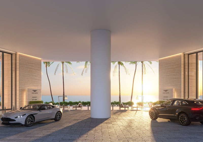 Aston Martin Residences in Downtown Miami luxury and ultra luxury condos symmetrical porte cochere dropoff with two luxury vehicles, palm trees, and sunset light by the water.