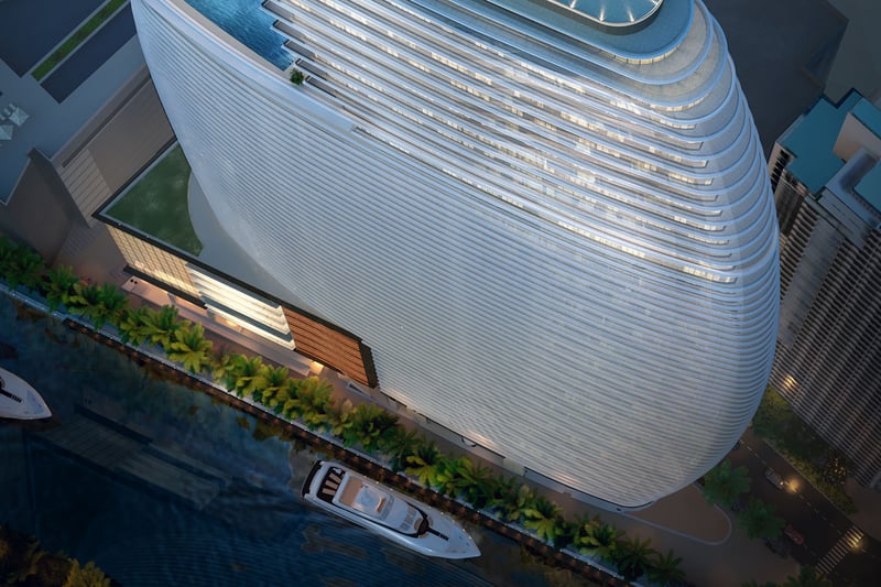 Aston Martin Residences in Downtown Miami luxury and ultra luxury condos top-down aerial of the curved waterfront tower with yachts, palm-lined frontage, and the rooftop pool deck.