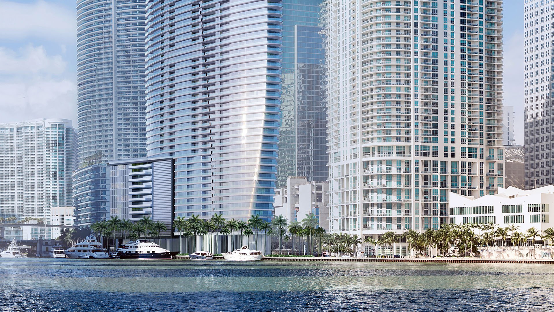 Aston Martin Residences in Downtown Miami luxury and ultra luxury condos waterfront facade seen across the water with yachts docked along the palm-lined shoreline.