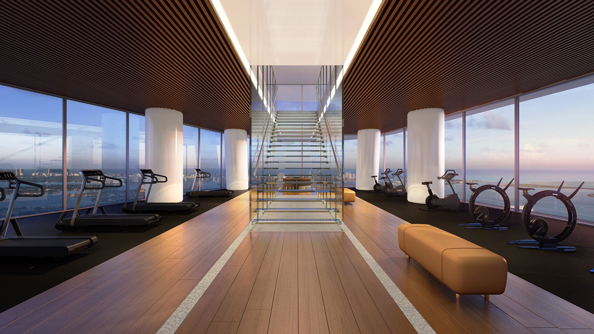 Aston Martin Residences in Downtown Miami luxury and ultra luxury condos waterfront fitness gallery with treadmills, bikes, and a central staircase framed by panoramic windows.