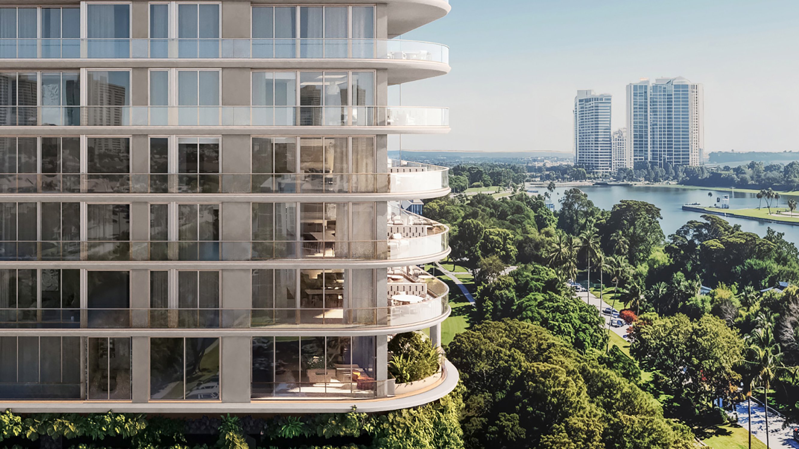 Avenia Aventura. Modern glass apartment building with curved balconies overlooking a river, trees, and tall buildings in the distance. Featuring lake.