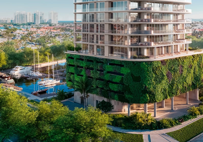 Avenia Aventura. Modern building with a green wall and balconies overlooks a marina with boats and a cityscape in the background. Featuring eco and friendly.
