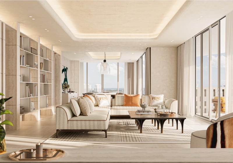Avenia Aventura. Modern, sunlit living room with cream sofas, a coffee table, bookshelves, large windows, and city views in a neutral color palette. Featuring interior design.