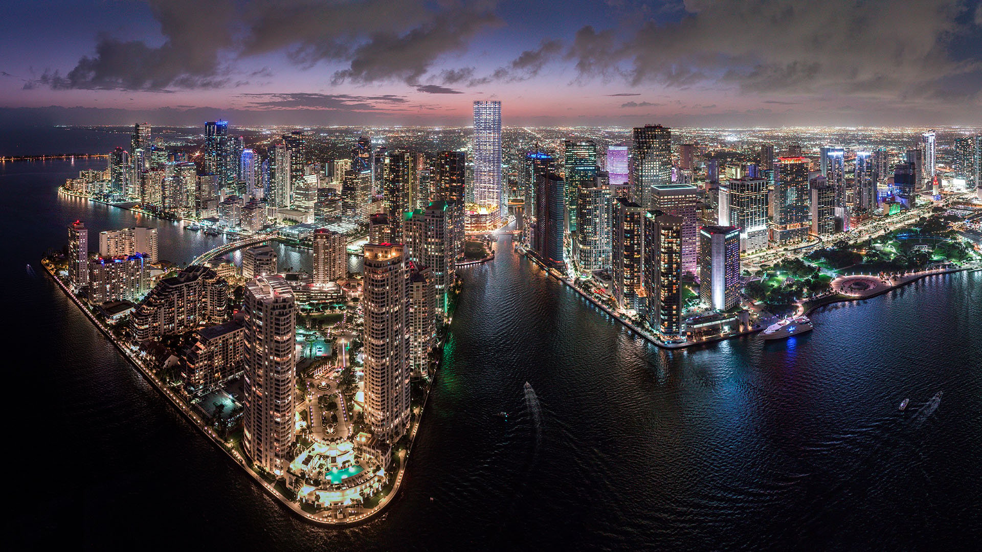 Baccarat Residences in Brickell, Miami, luxury and ultra luxury condos featuring a twilight aerial of the riverfront skyline, illuminated towers, waterfront streets, and glowing city lights.