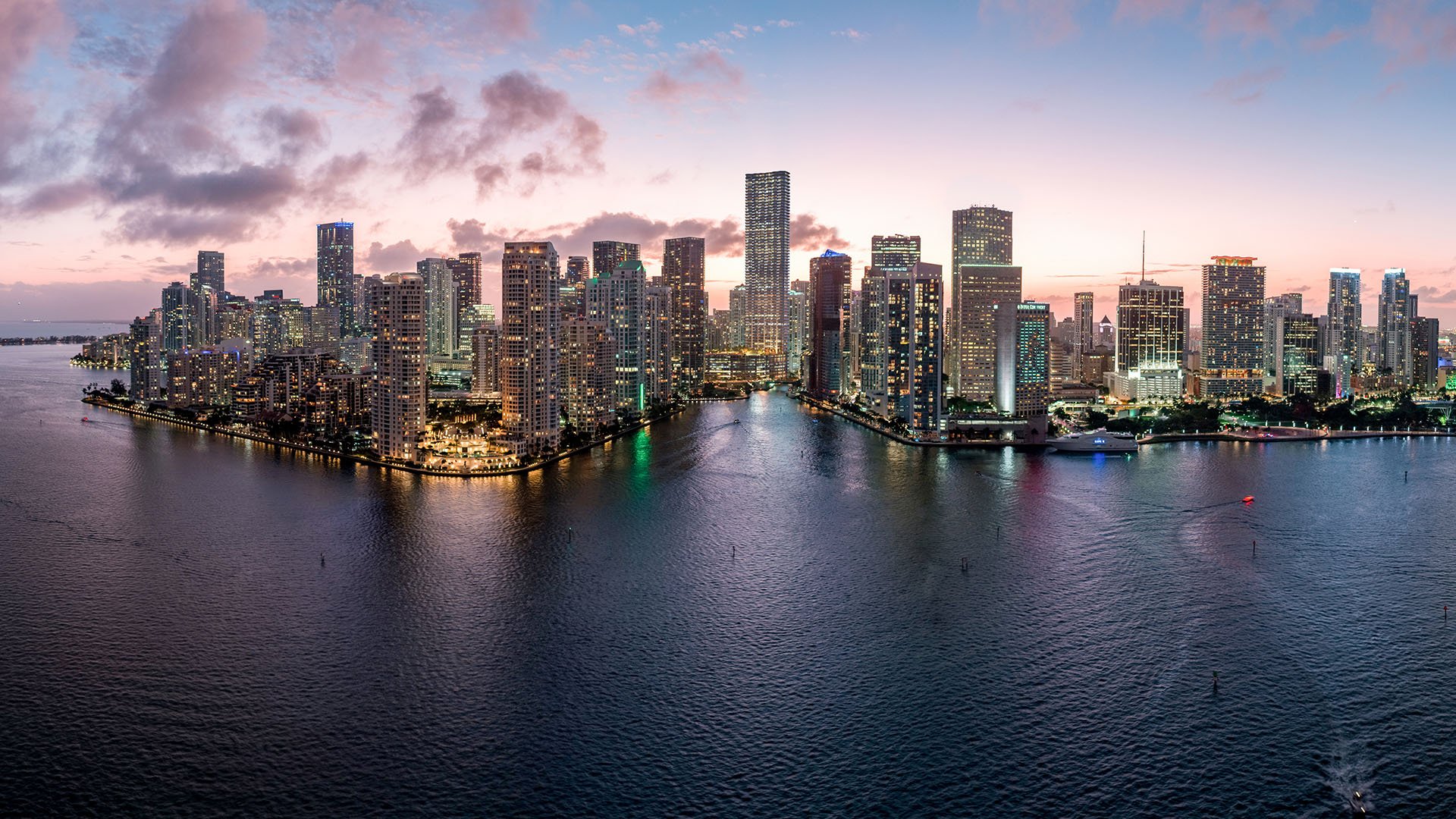 Baccarat Residences in Brickell, Miami, luxury and ultra luxury condos featuring a panoramic dusk view of the bayfront skyline, glowing towers, and open water in the foreground.