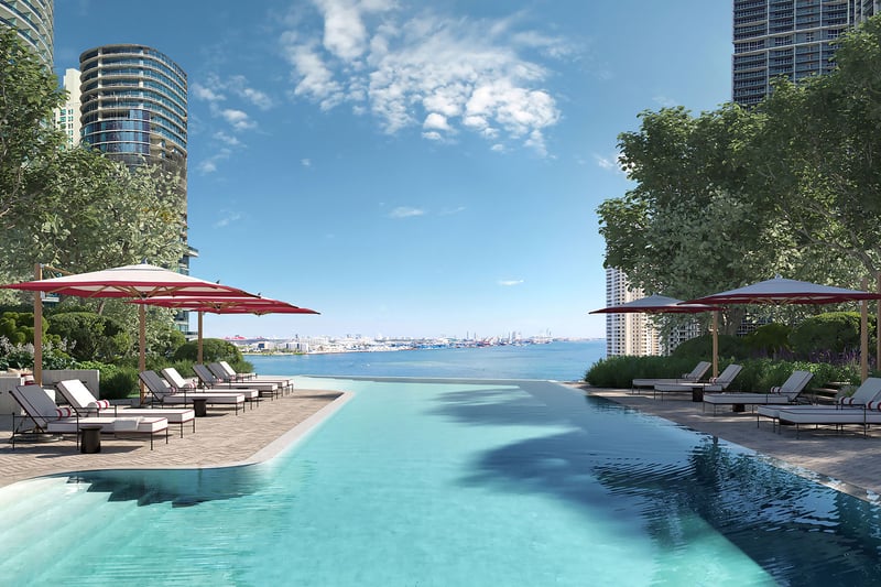 Baccarat Residences in Brickell, Miami, luxury and ultra luxury condos featuring a waterfront pool terrace, red umbrellas, sun loungers, landscaped edges, and open bay views.