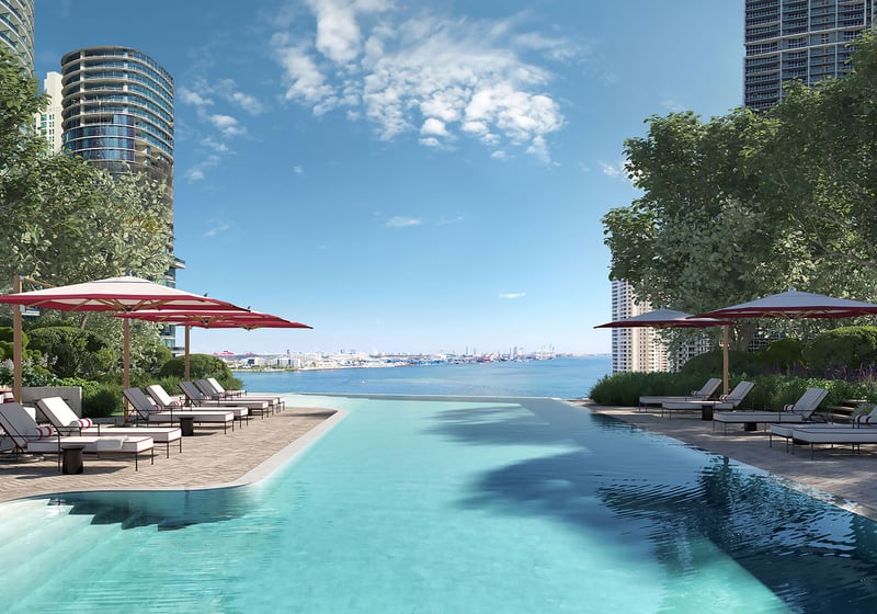 Baccarat Residences in Brickell, Miami, luxury and ultra luxury condos featuring a waterfront pool terrace, red umbrellas, sun loungers, landscaped edges, and open bay views.