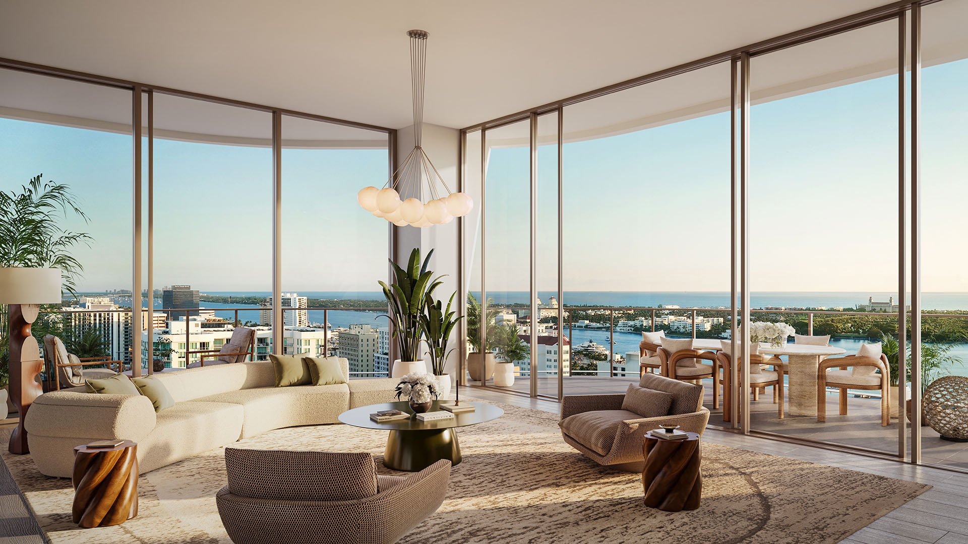 Wraparound great room with curved seating, floor-to-ceiling glass, and a terrace overlooking the water at Banyan Tree Residences in West Palm Beach, highlighting luxury and ultra luxury condos with expansive indoor outdoor living.