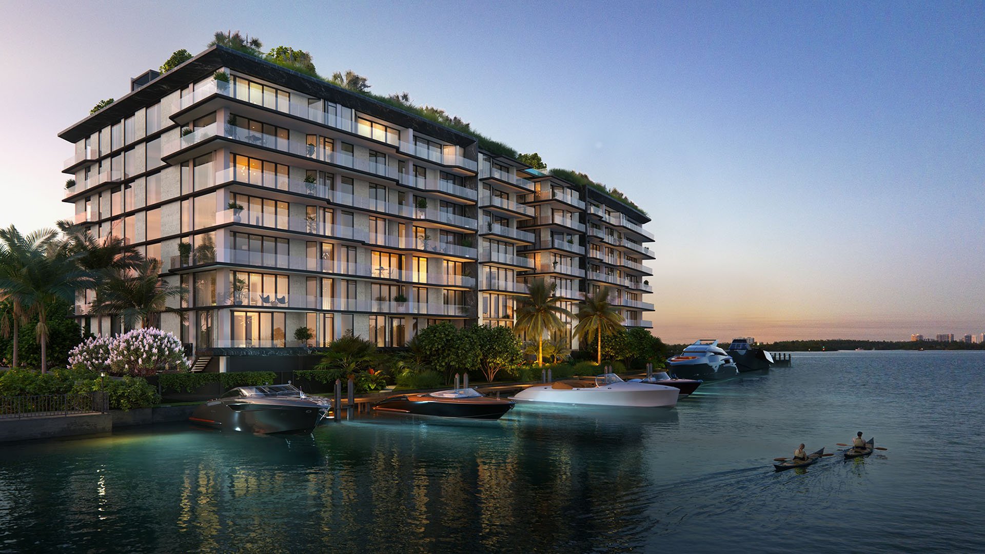 Sunset waterfront exterior of Bay Harbor Towers, Bay Harbor Islands, Florida with marina dock, yachts and illuminated glass balconies, promoting luxury and ultra luxury preconstruction condos on the bay.