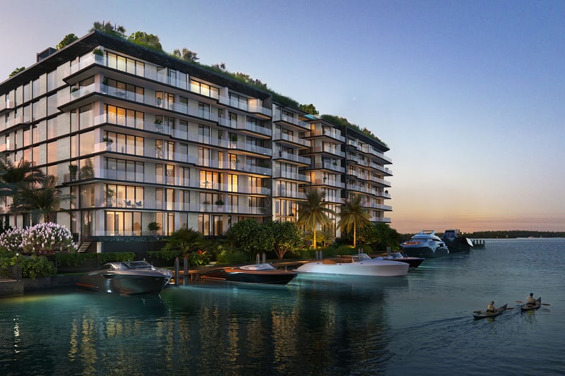 Sunset waterfront exterior of Bay Harbor Towers, Bay Harbor Islands, Florida with marina dock, yachts and illuminated glass balconies, promoting luxury and ultra luxury preconstruction condos on the bay.