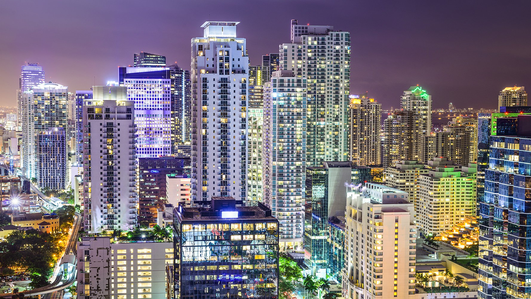 Brickell, Miami night cityscape with illuminated towers over Biscayne Bay—ultra luxury and luxury condos dominate, with preconstruction and resale opportunities.