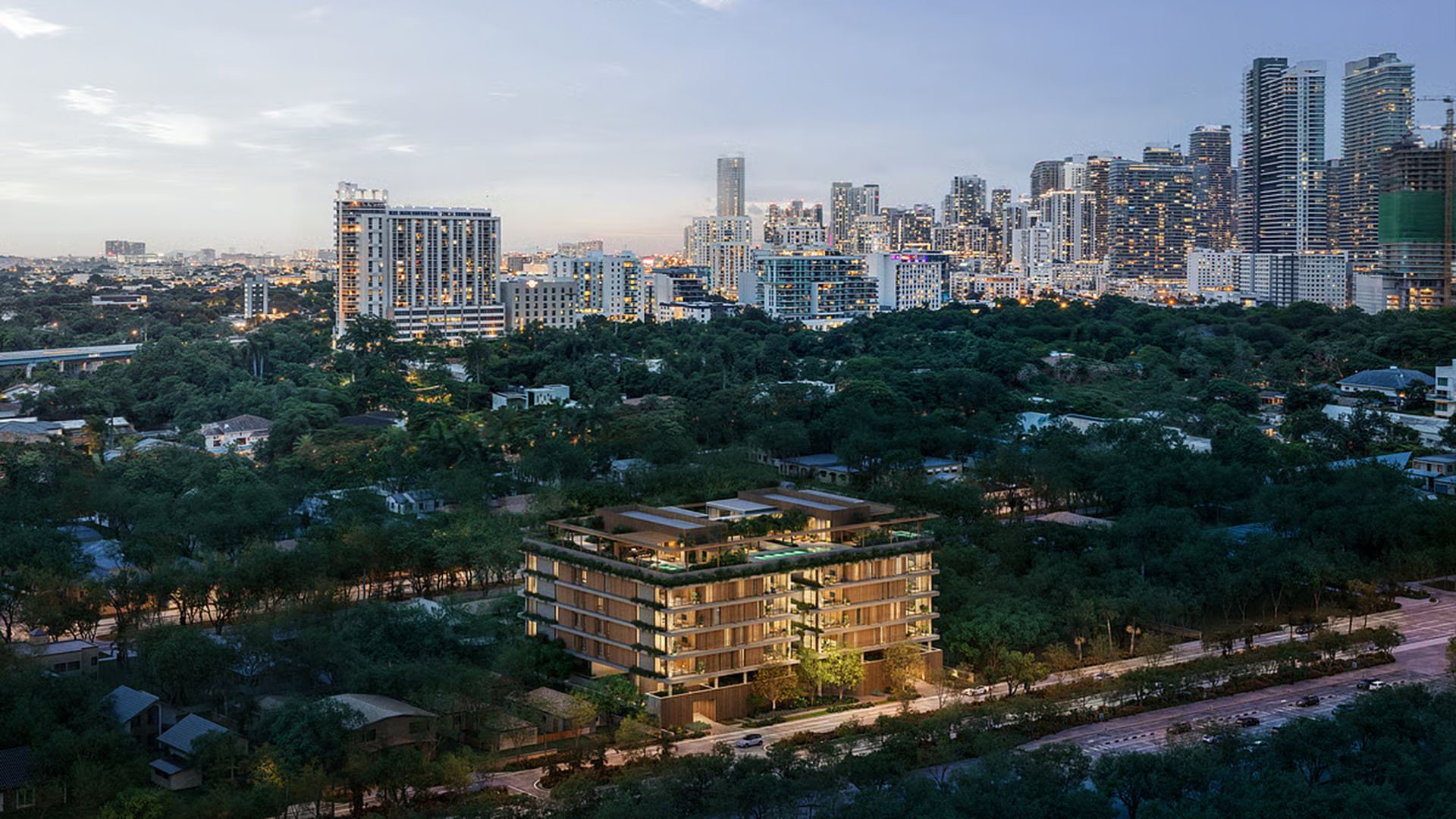 Colette Residences in Brickell luxury ultra luxury condos seen from above at dusk, with the mid-rise building illuminated amid lush greenery and the skyline in the background.