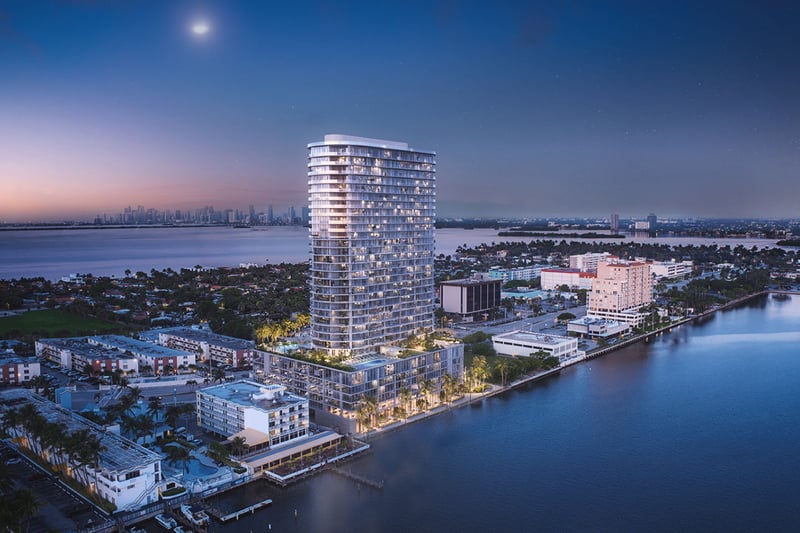 Aerial waterfront view of the curved tower and distant skyline at Continuum Club and Residences in North Bay Village, a preconstruction luxury and ultra luxury condos development set along the bay at twilight.