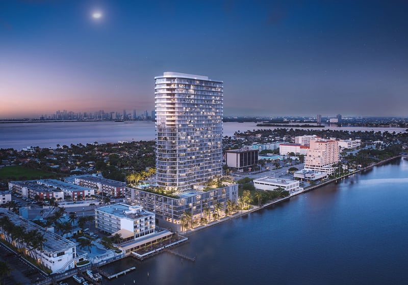 Aerial waterfront view of the curved tower and distant skyline at Continuum Club and Residences in North Bay Village, a preconstruction luxury and ultra luxury condos development set along the bay at twilight.