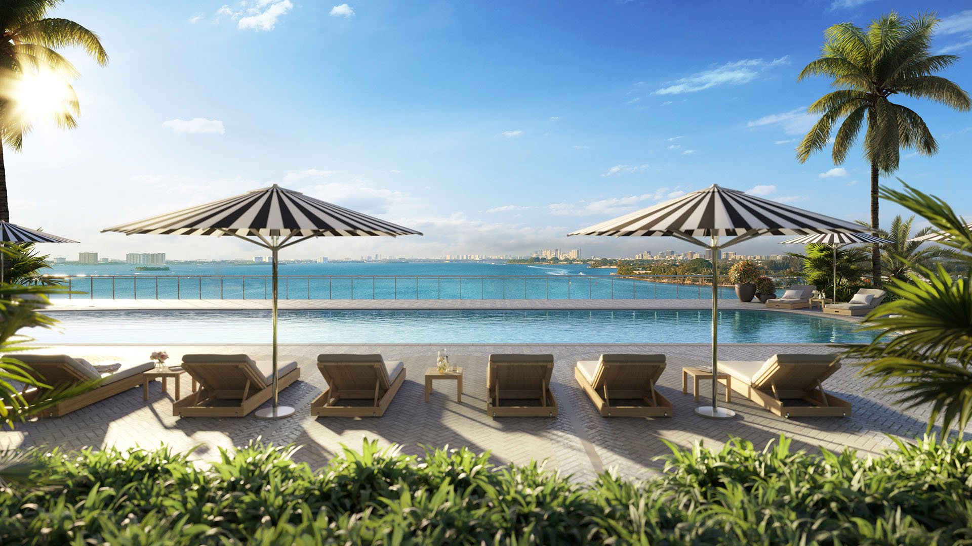 Infinity pool with striped umbrellas, sun loungers, and bay views at Continuum Club and Residences in North Bay Village, a preconstruction luxury and ultra luxury condos development with resort-style waterfront amenities.