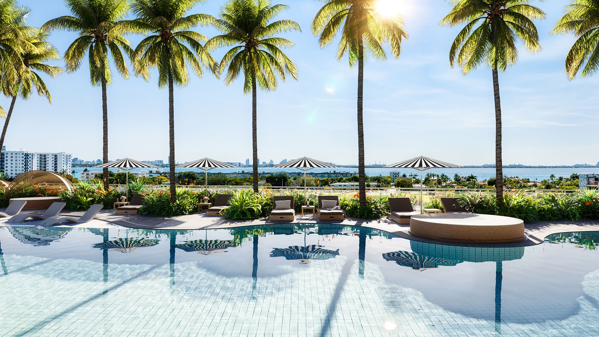 Palm-lined resort pool terrace with loungers and shallow water reflections at Continuum Club and Residences in North Bay Village, a preconstruction luxury and ultra luxury condos development with tropical waterfront amenities.