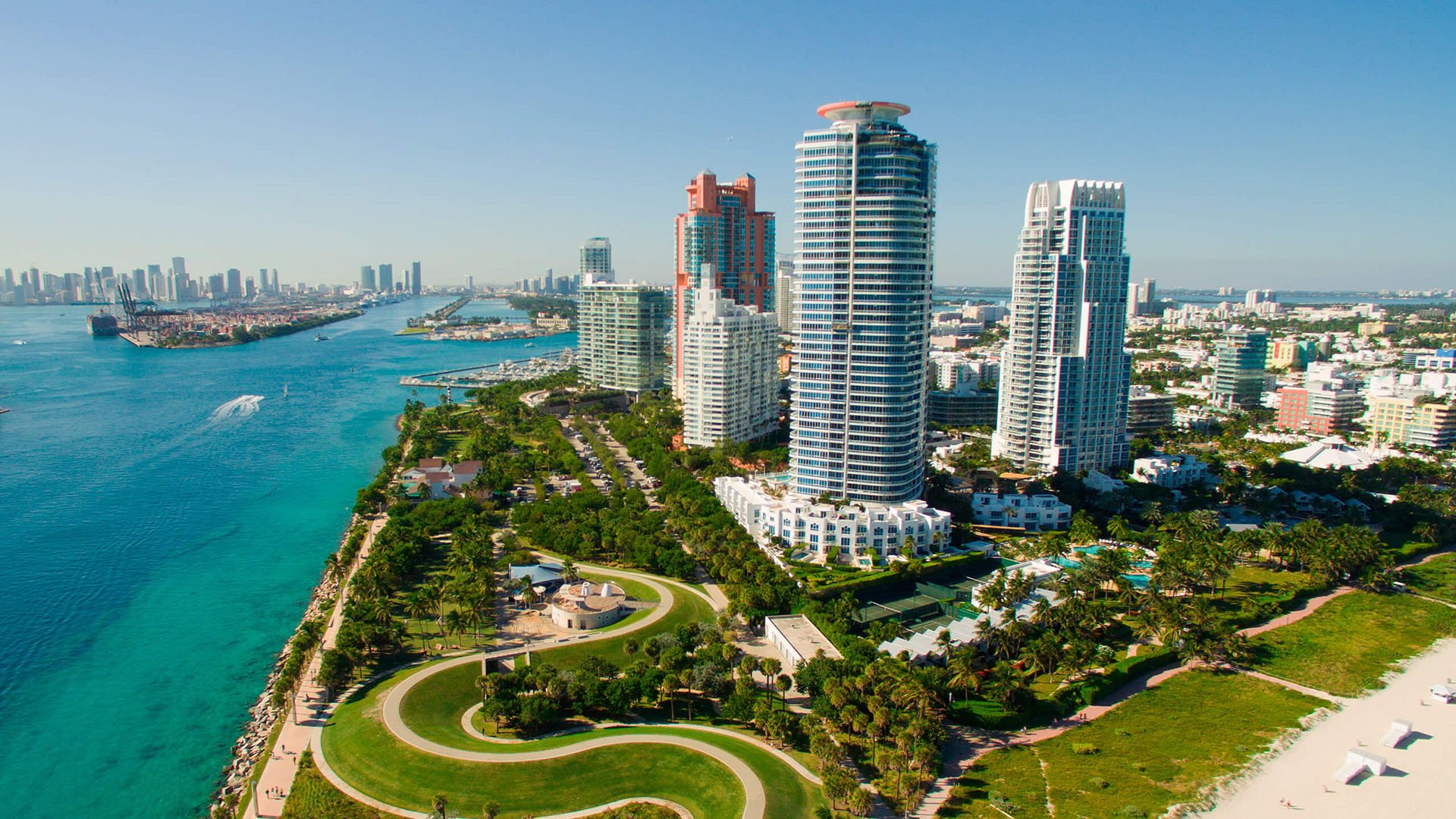 Aerial waterfront view of Continuum on South Beach, Miami Beach, Florida, with luxury and ultra luxury condos beside a sweeping coastal park, turquoise inlet water, and the surrounding skyline.