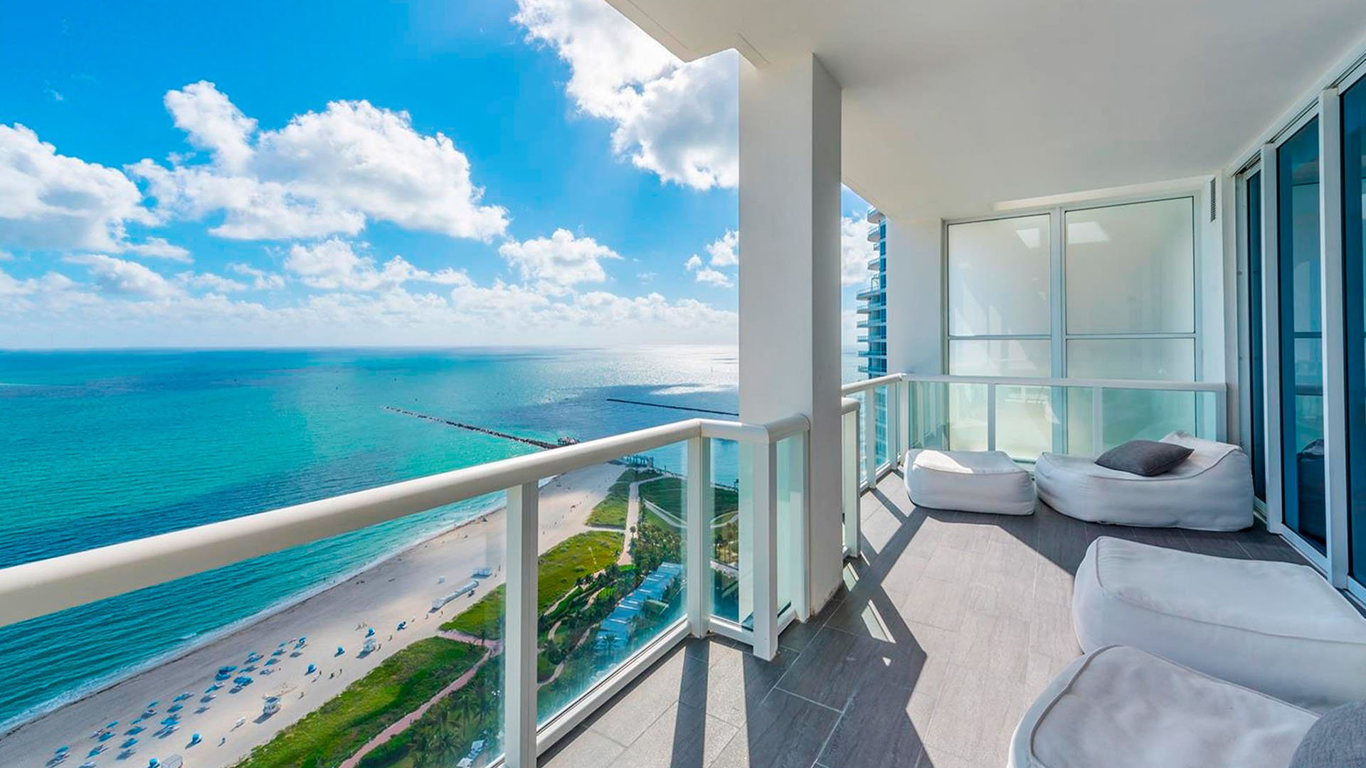 Oceanfront balcony at Continuum on South Beach, Miami Beach, Florida, complementing luxury and ultra luxury condos with chaise lounges, glass railings, a sweeping beach view, and bright turquoise water.