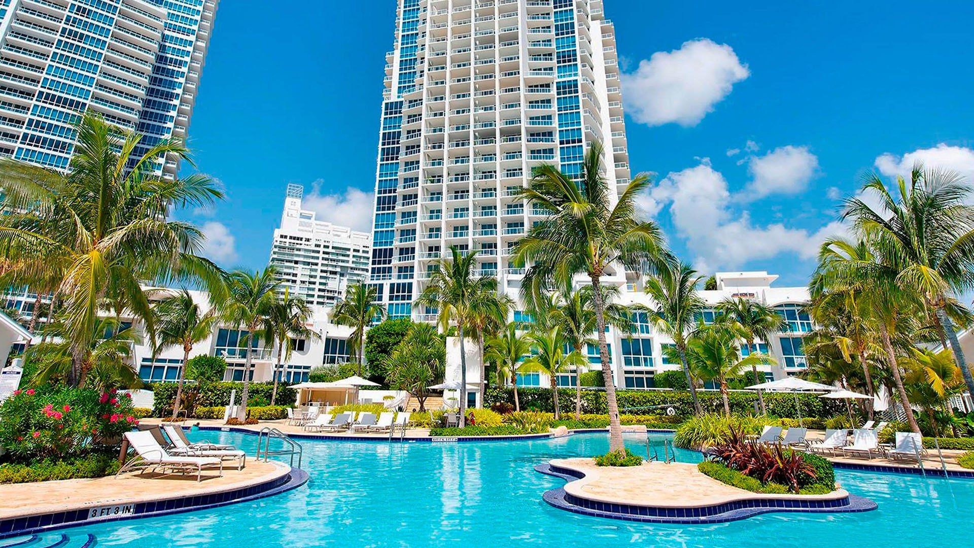 Resort pool deck at Continuum on South Beach, Miami Beach, Florida, serving luxury and ultra luxury condos with tropical palms, lounge seating, curving water edges, and tall tower views.