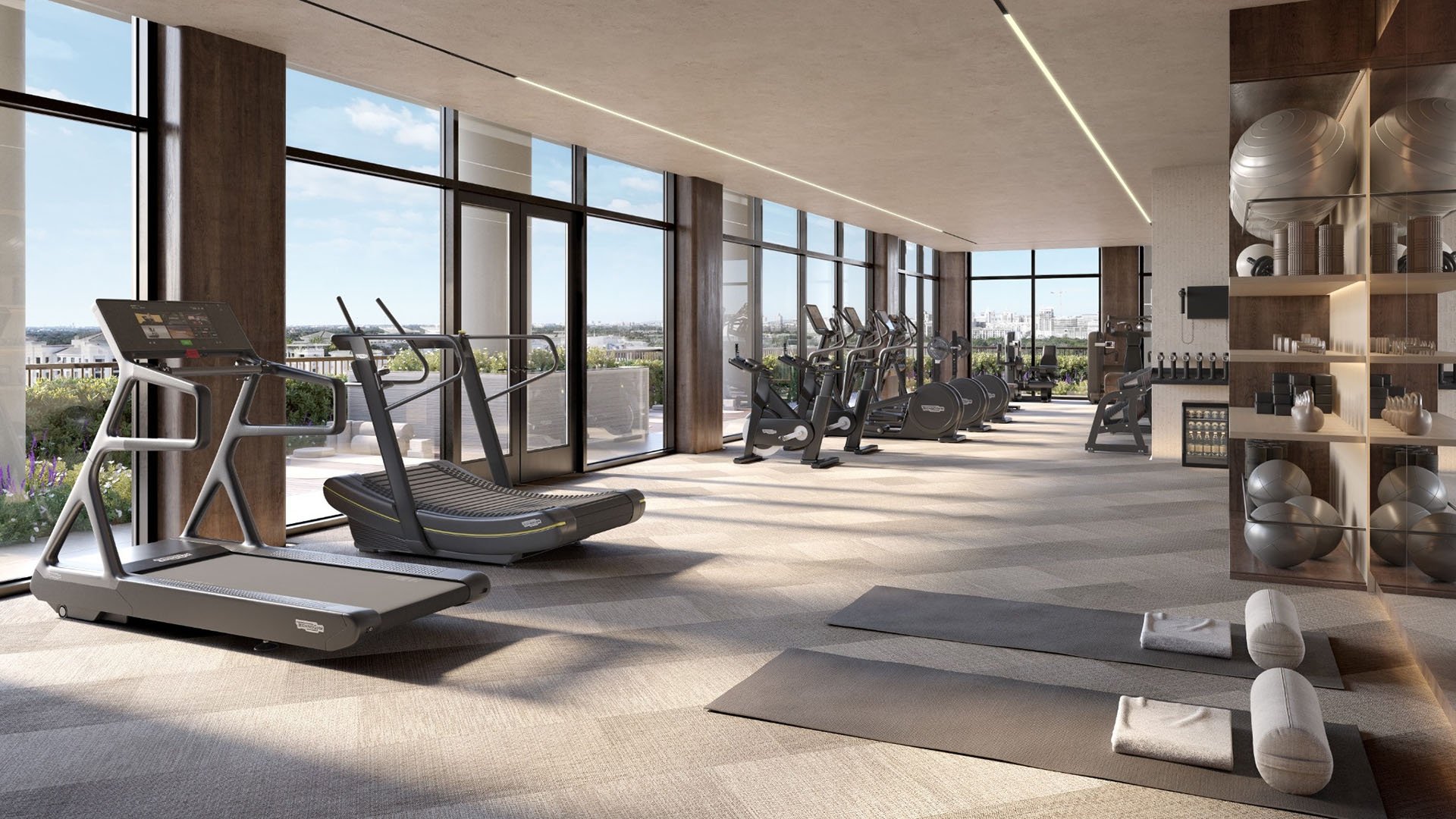 Fitness center with treadmills, bikes, yoga mats, and floor-to-ceiling glass at Cora Merrick Park in Coral Gables, an amenity for luxury and ultra luxury condos with bright skyline views.