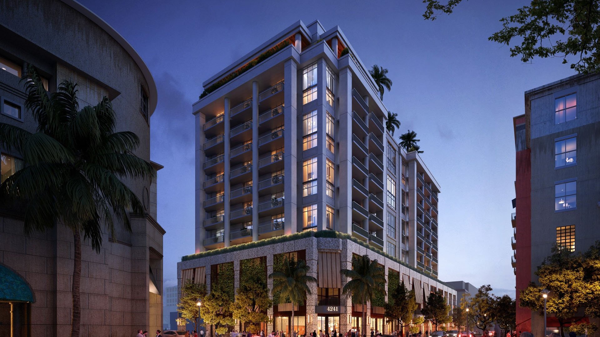 Twilight view of the illuminated condo tower at Cora Merrick Park in Coral Gables, rising above retail and palms with a refined facade for luxury and ultra luxury condos.