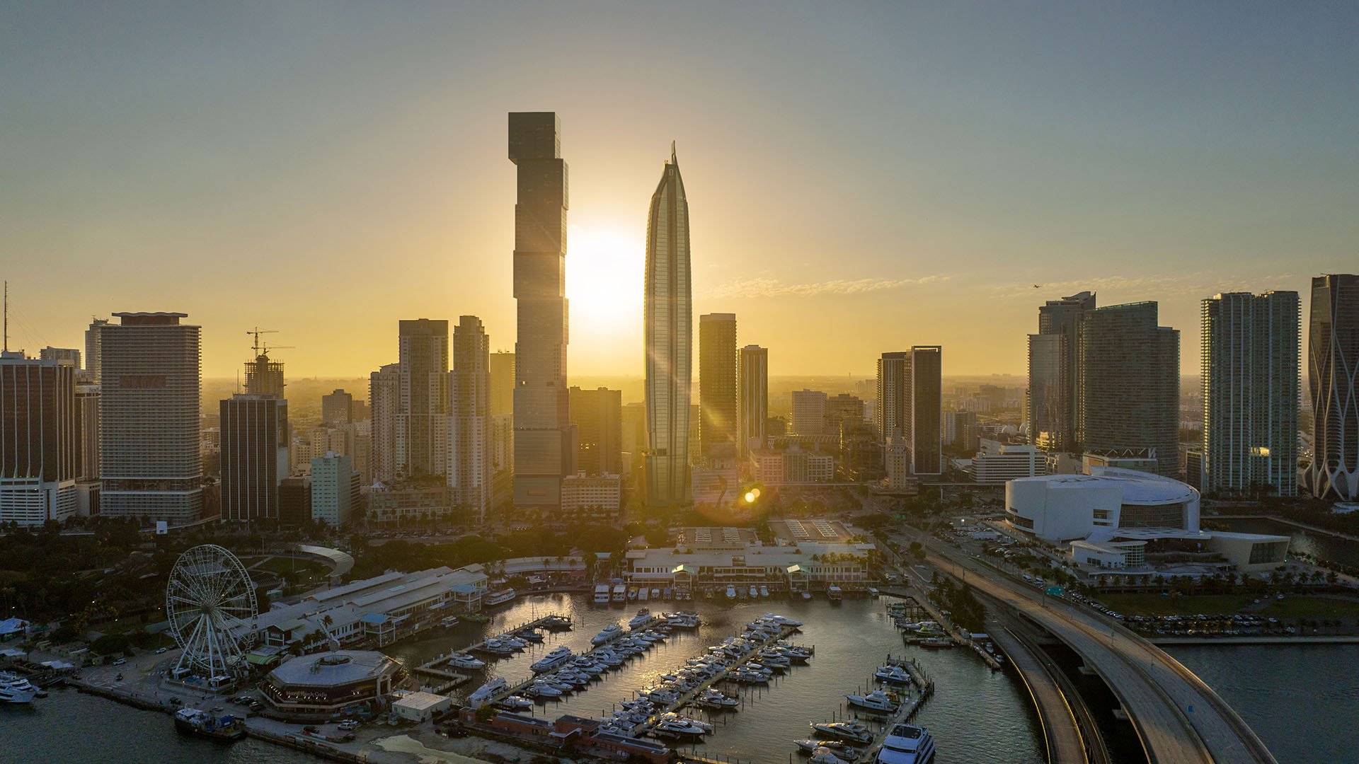 Aerial sunrise skyline view at Delano Residences & Hotel, Miami, with a marina, bridge, and surrounding high-rise towers, showing luxury and ultra luxury preconstruction condos on the waterfront.