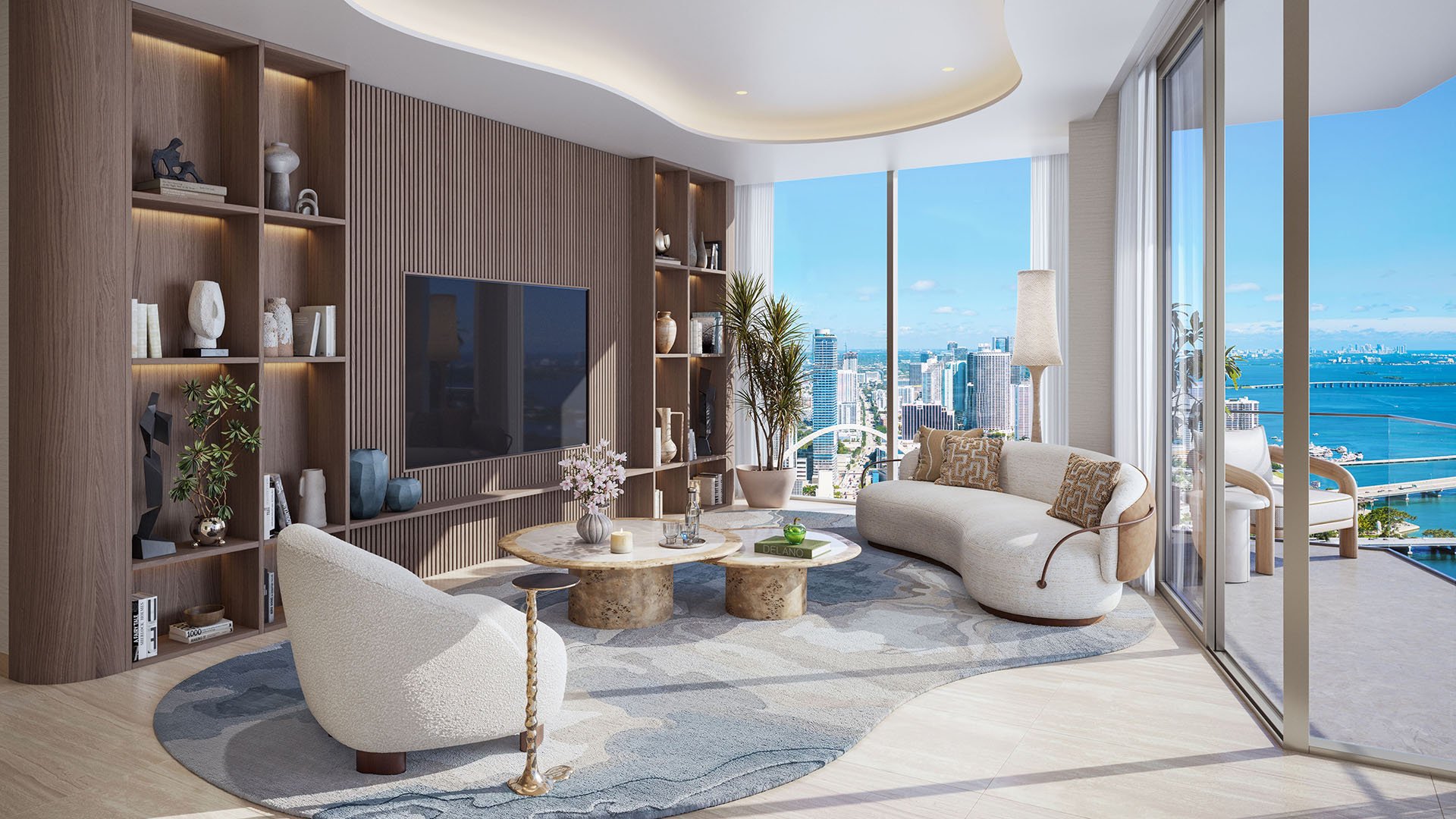 Great room at Delano Residences & Hotel, Miami, with a curved sofa, built-in shelving, floor-to-ceiling glass, and balcony bay views, showing luxury and ultra luxury preconstruction condos.