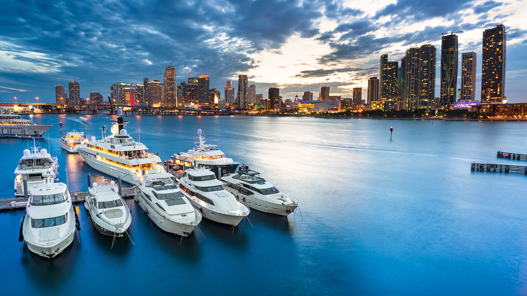 Downtown Miami marina at sunset with glowing skyline and yachts, iconic hub for luxury and ultra luxury condos, offering preconstruction and resale.
