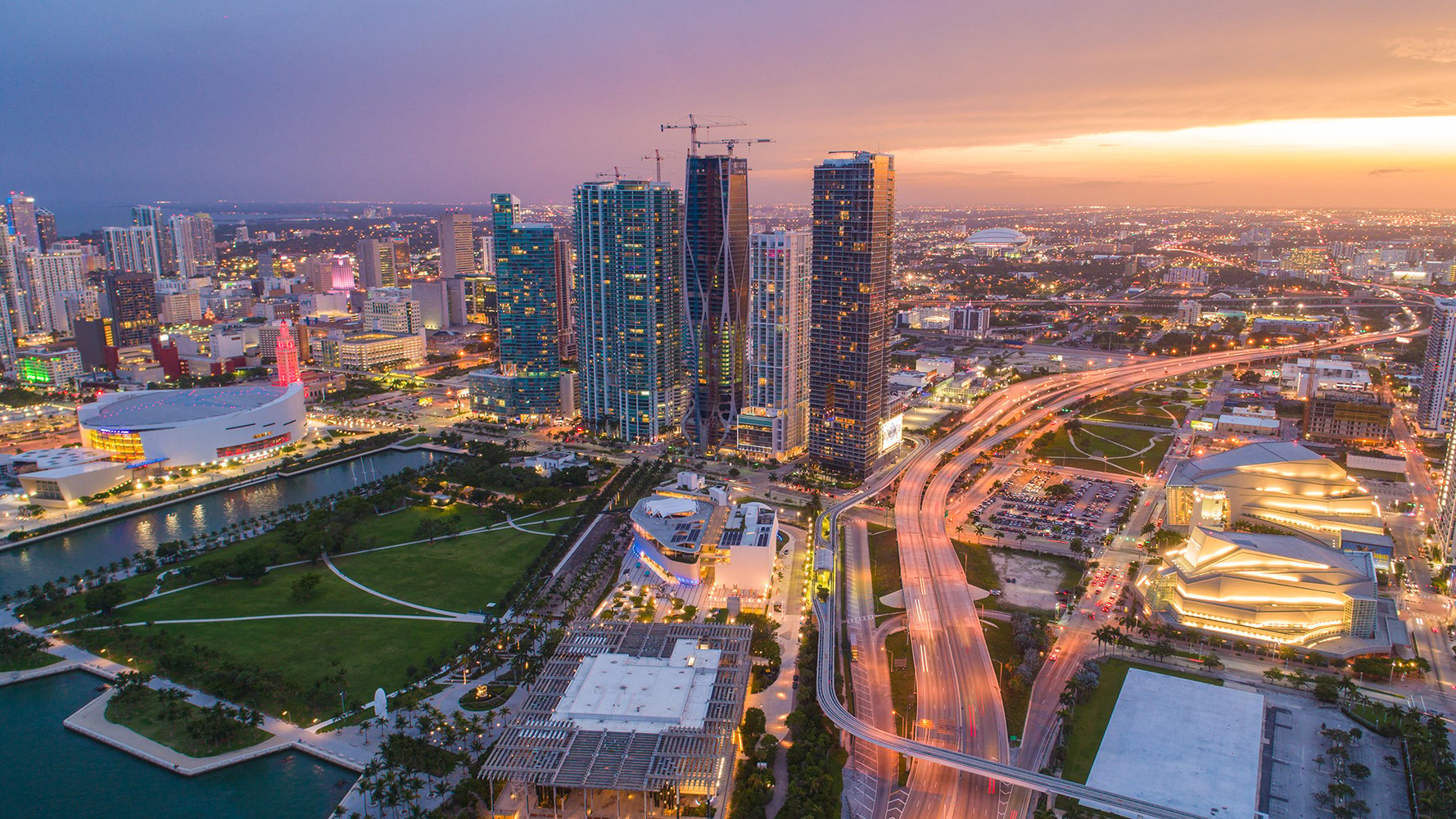 Downtown Miami skyline at sunset with pastel sky and bay reflections—hub for luxury and ultra luxury condos, preconstruction and resale listings.