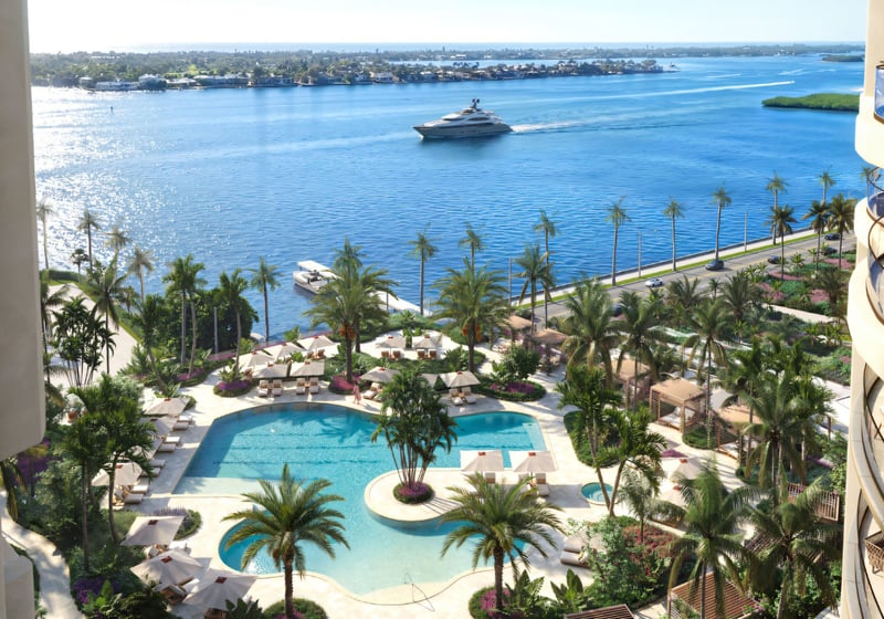 Edgeworth West Palm Beach luxury ultra luxury condos amenity deck overlooking the waterfront, with a resort-style pool, palm-lined terraces, lounge seating, and a marina view with a yacht passing by.