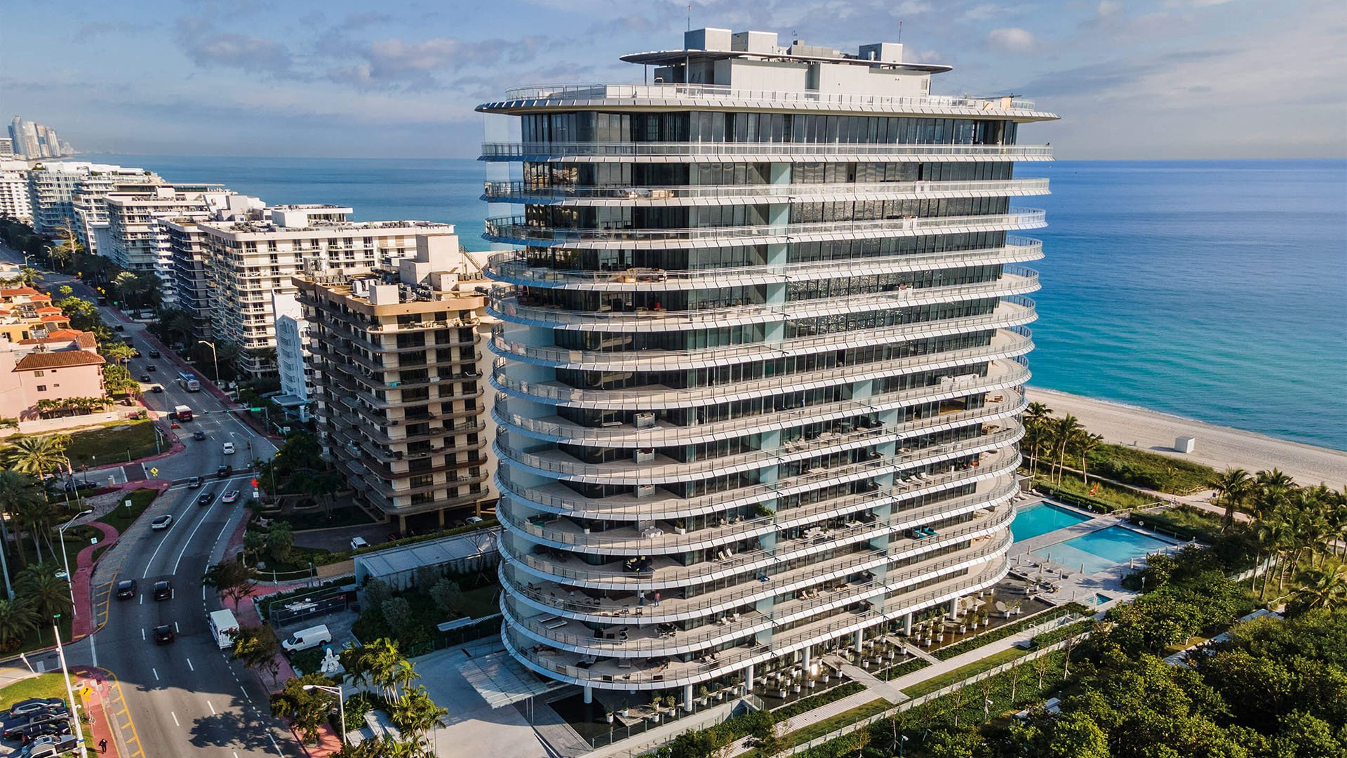 Eighty Seven Park, Miami Beach luxury and ultra luxury condos tower seen from the air beside the beach, ocean, and coastal road, with the pool deck and neighboring buildings below.