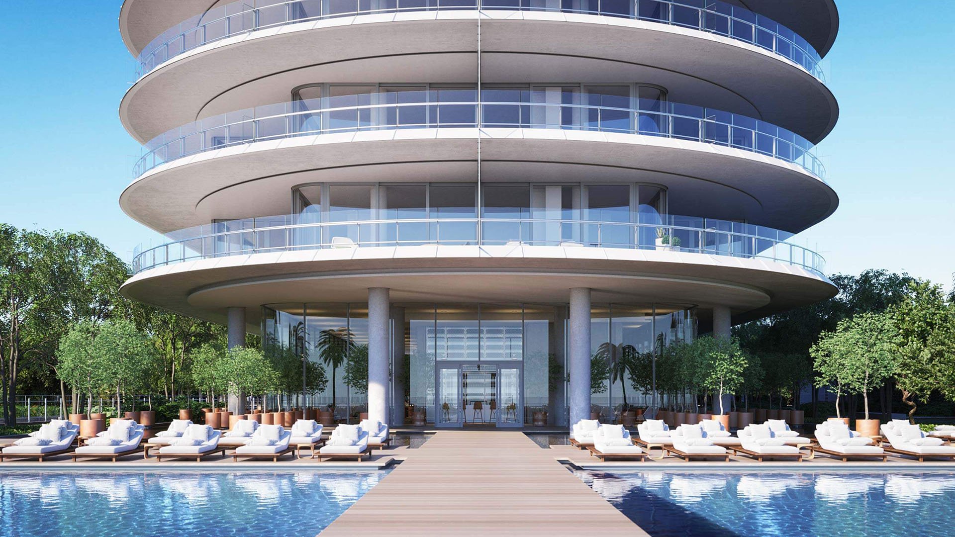 Eighty Seven Park, Miami Beach luxury and ultra luxury condos arrival view with a curved glass facade, grand entry, reflective pool, and rows of resort-style loungers.