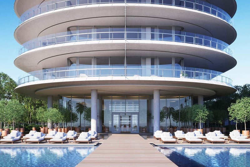 Eighty Seven Park, Miami Beach luxury and ultra luxury condos arrival view with a curved glass facade, grand entry, reflective pool, and rows of resort-style loungers.