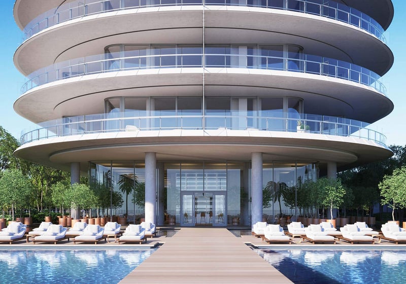 Eighty Seven Park, Miami Beach luxury and ultra luxury condos arrival view with a curved glass facade, grand entry, reflective pool, and rows of resort-style loungers.
